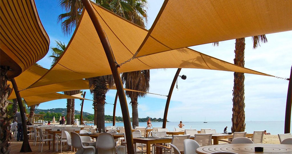 Sail Shades on a beach setting with tables and chairs